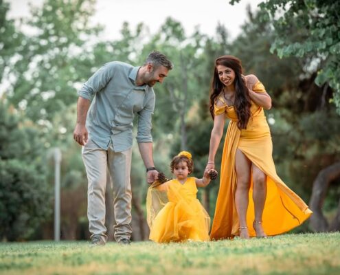 Γονείς περπατούν κρατώντας από το χέρι το μικρό κοριτσάκι τους που φοράει κίτρινο φόρεμα.