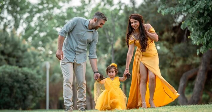 Γονείς περπατούν κρατώντας από το χέρι το μικρό κοριτσάκι τους που φοράει κίτρινο φόρεμα.