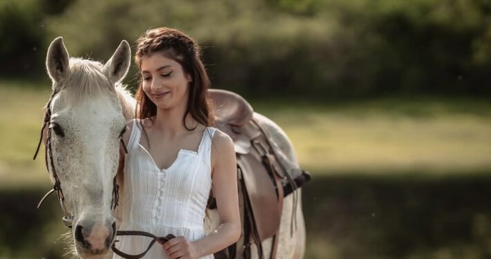 Η νύφη στέκεται δίπλα σε ένα λευκό άλογο στη φύση.