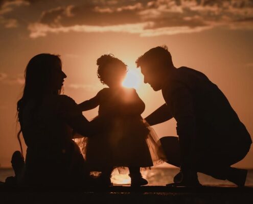 Καλλιτεχνική φωτογραφία με τις σιλουέτες των γονιών και του παιδιού τους μπροστά στο ηλιοβασίλεμα.