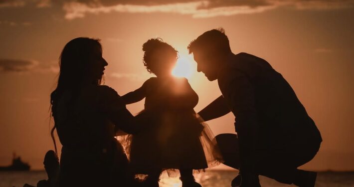 Καλλιτεχνική φωτογραφία με τις σιλουέτες των γονιών και του παιδιού τους μπροστά στο ηλιοβασίλεμα.