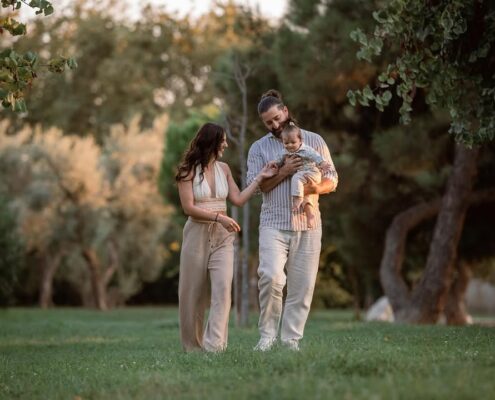Οικογένεια περπατάει ανέμελα στο πάρκο, με τον πατέρα να κρατάει το μωρό αγκαλιά.