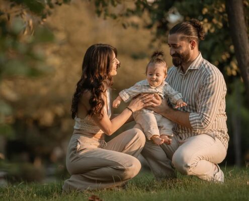 Γονείς κάθονται στο γρασίδι και χαμογελούν μαζί με το μωρό τους.