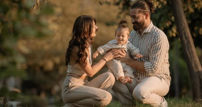 Γονείς κάθονται στο γρασίδι και χαμογελούν μαζί με το μωρό τους.
