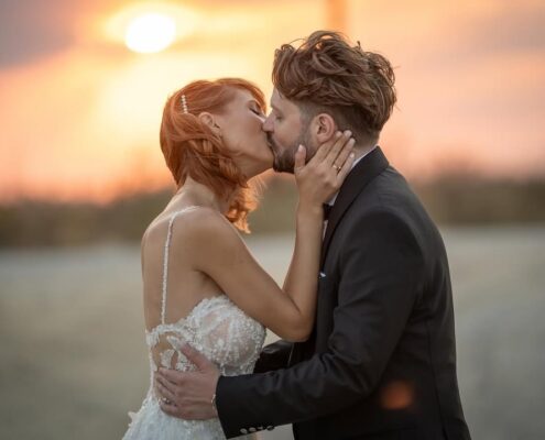 Ρομαντικό πορτραίτο του ζευγαριού που φιλιέται με φόντο το ζεστό φως του ηλιοβασιλέματος.