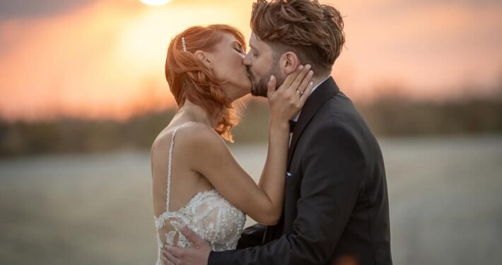 Ρομαντικό πορτραίτο του ζευγαριού που φιλιέται με φόντο το ζεστό φως του ηλιοβασιλέματος.