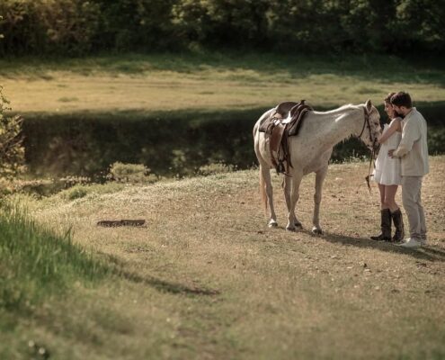 Φωτογράφιση του ζευγαριού μετά τον γάμο σε καταπράσινο τοπίο με ένα λευκό άλογο.