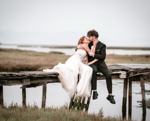 Το ζευγάρι κάθεται σε μια ξύλινη αποβάθρα δίπλα στο νερό και ανταλλάσσει ένα φιλί.