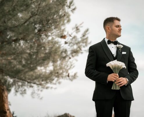 Ο γαμπρός με μαύρο κοστούμι κρατάει τη νυφική ανθοδέσμη σε εξωτερικό χώρο.