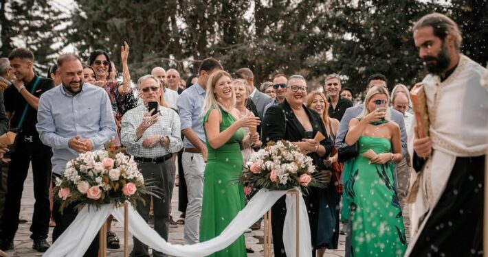 Οι καλεσμένοι του γάμου παρακολουθούν και χειροκροτούν κατά τη διάρκεια της υπαίθριας τελετής.