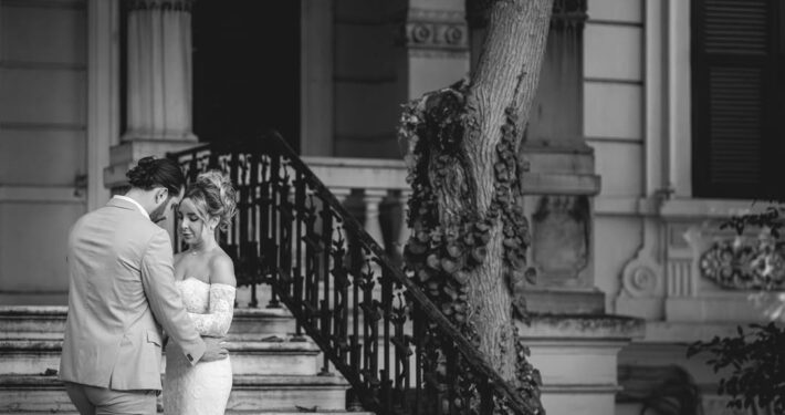 Το ζευγάρι στέκεται δίπλα σε πέτρινα σκαλιά σε μια ατμοσφαιρική ασπρόμαυρη λήψη.