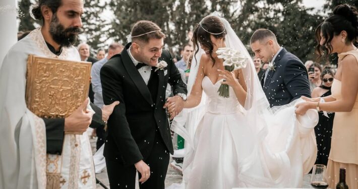 Ο γαμπρός φιλάει το χέρι της νύφης κατά τη διάρκεια της γαμήλιας τελετής σε εξωτερικό χώρο.