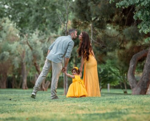 Οικογένεια περπατάει στο γρασίδι, με τους γονείς να ανταλλάσσουν ένα φιλί και το παιδί να προπορεύεται.