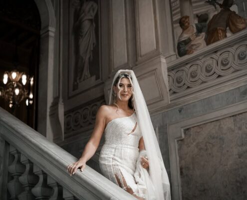 Η νύφη με το νυφικό της στέκεται στα σκαλιά μιας μεγαλοπρεπούς μαρμάρινης σκάλας.