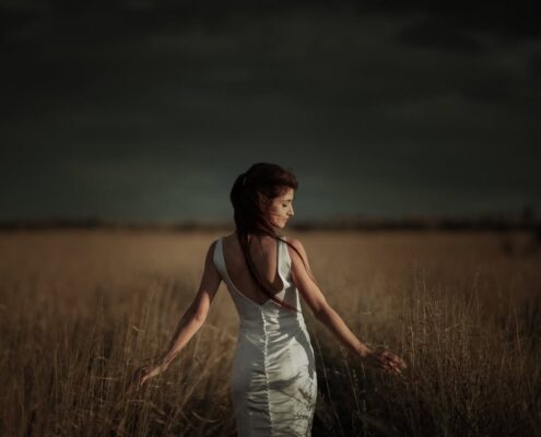 Κινηματογραφική λήψη της νύφης να περπατάει σε χωράφι κάτω από συννεφιασμένο ουρανό.