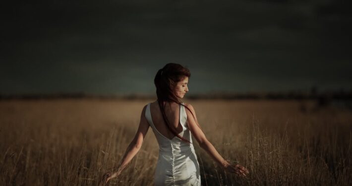 Κινηματογραφική λήψη της νύφης να περπατάει σε χωράφι κάτω από συννεφιασμένο ουρανό.