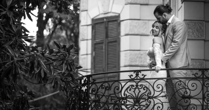 Ασπρόμαυρη φωτογραφία του ζευγαριού σε μπαλκόνι κτιρίου με νεοκλασική αισθητική.