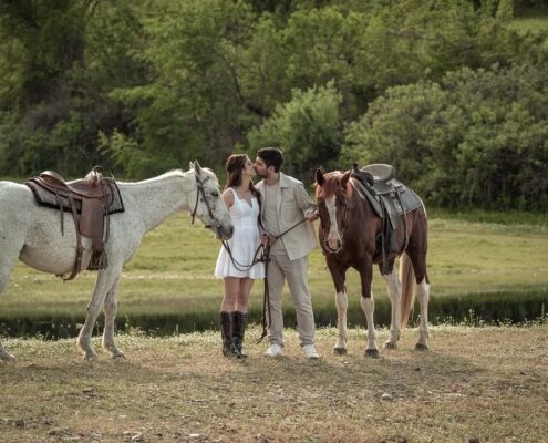 Το ζευγάρι ποζάρει με τα άλογά του σε ένα καταπράσινο φυσικό τοπίο.