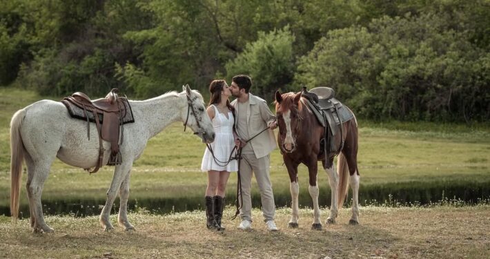 Το ζευγάρι ποζάρει με τα άλογά του σε ένα καταπράσινο φυσικό τοπίο.