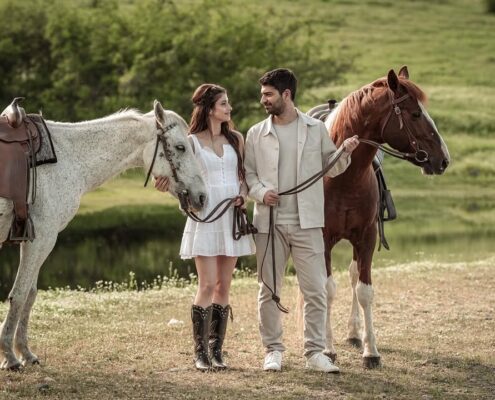 Ο γαμπρός και η νύφη περπατούν χαλαροί στο γρασίδι δίπλα στα άλογα.
