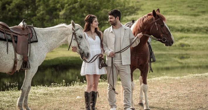Ο γαμπρός και η νύφη περπατούν χαλαροί στο γρασίδι δίπλα στα άλογα.