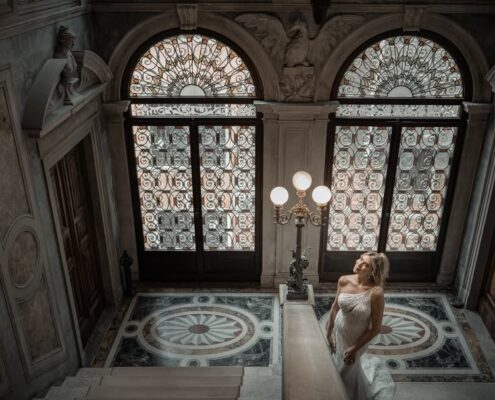 Γάμος στην Βενετία. Η νύφη ποζάρει δίπλα σε μια μεγάλη περίτεχνη πόρτα με βιτρό σε ένα εντυπωσιακό κτίριο.